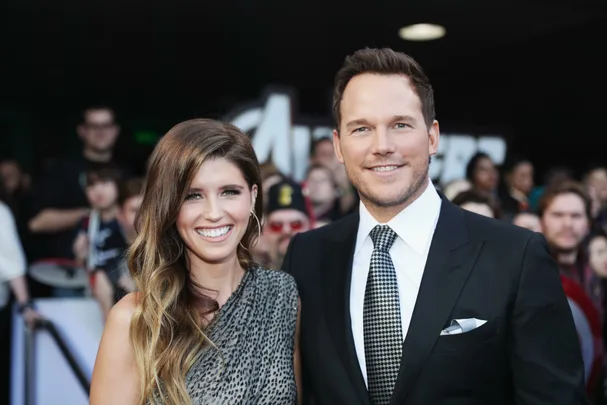 A smiling couple poses on the red carpet at a movie premiere, surrounded by other attendees.