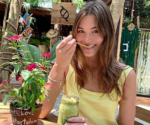 Woman enjoying a green smoothie in an outdoor cafe, with vibrant plants around.