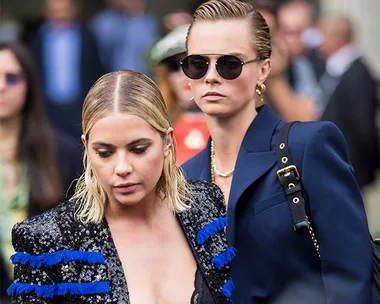 Two women walking together at an event, one in a blue blazer and sunglasses, the other in a patterned outfit with blue accents.