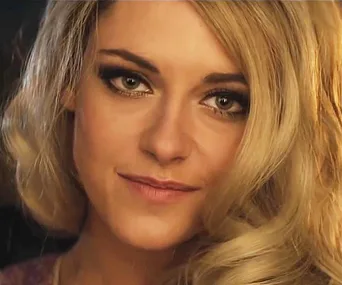 A woman with blonde hair and smoky eye makeup, smiling softly in a close-up shot.