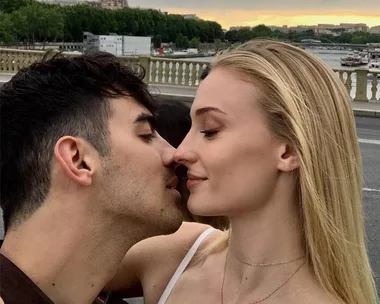 A couple sharing a close, intimate moment on a bridge, with scenic views of the river and cityscape in the background.