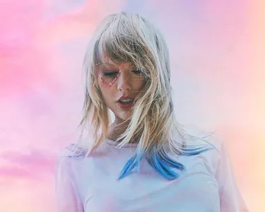 Singer with blonde hair, wearing a white top, pink heart around eye, against a pastel sky background.