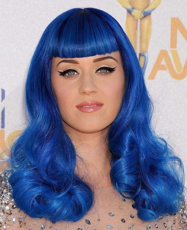 Woman with bright blue hair and bangs, wearing a sparkly outfit, posing at an event.