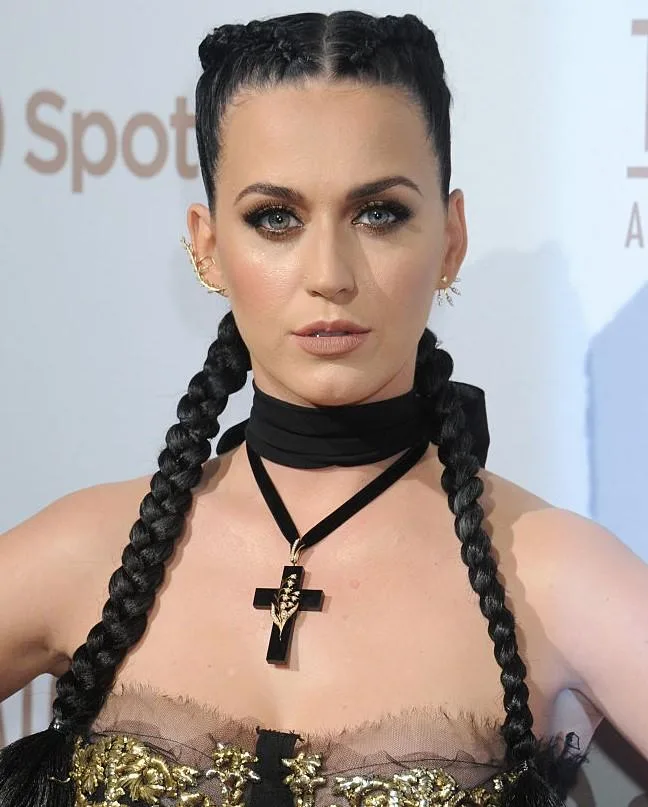 Katy Perry in a braided hairstyle, wearing a black cross necklace, attends an event.