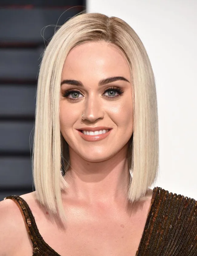 A person with blonde hair and a nose ring, wearing a brown dress, smiling at an event.