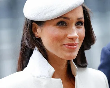 Woman in a white beret and coat, smiling and looking to the side.