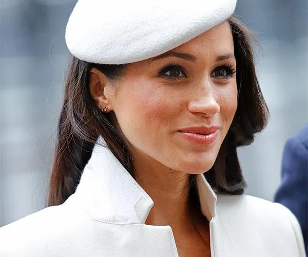 Woman in a white beret and coat, smiling and looking to the side.