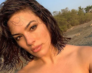 Woman with wet hair and natural makeup taking a selfie on a beach.