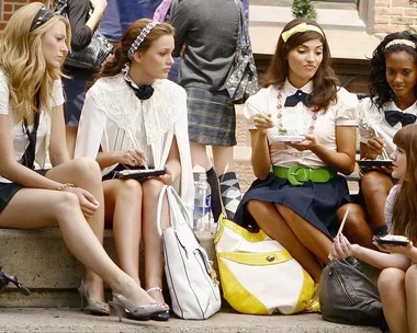 A group of young women, dressed in school uniforms, sit on steps outdoors in a scene from "Gossip Girl."