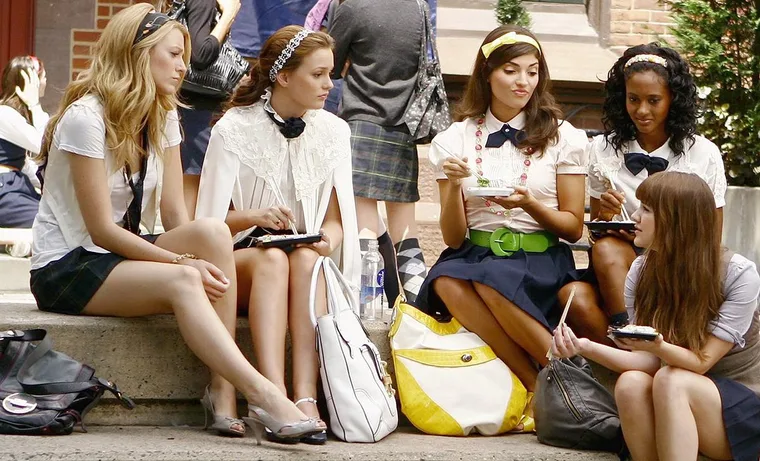 A group of young women, dressed in school uniforms, sit on steps outdoors in a scene from "Gossip Girl."