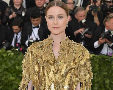 Evan Rachel Wood in a gold feathered outfit at a formal event with photographers in the background.