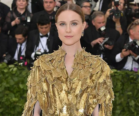 Evan Rachel Wood in a gold feathered outfit at a formal event with photographers in the background.