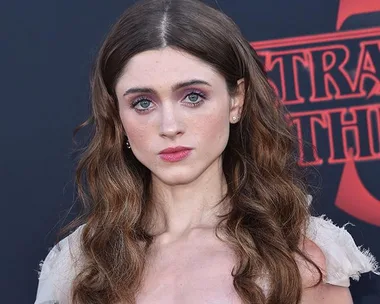 Woman with long brown hair, wearing a light dress, stands in front of a "Stranger Things" promotional backdrop.