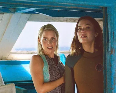 Two women in wetsuits stand on a boat, looking outward, possibly from a scene in the film "47 Meters Down".