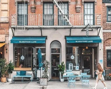 Facade of Bluestone Lane café in New York, with teal awnings and outdoor seating on the sidewalk.