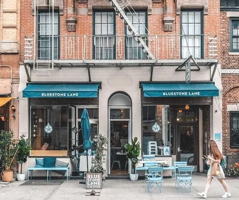 Facade of Bluestone Lane café in New York, with teal awnings and outdoor seating on the sidewalk.