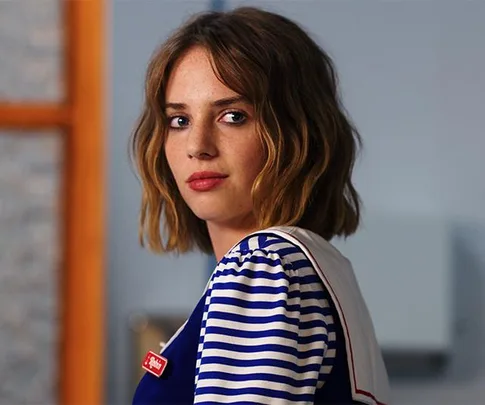 Young woman in a blue and white striped uniform, looking sideways, possibly a character from a popular Netflix show.