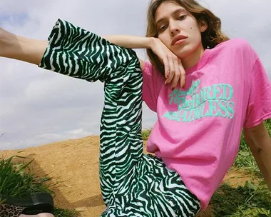 Person in pink shirt with green zebra-striped pants seated relaxed outdoors.