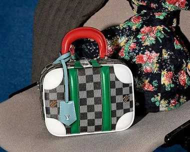 Louis Vuitton checkered handbag with red handle, green stripes, and blue tag on floral fabric background.