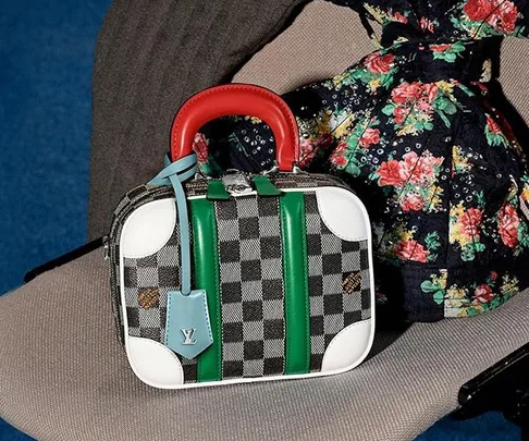 Louis Vuitton checkered handbag with red handle, green stripes, and blue tag on floral fabric background.