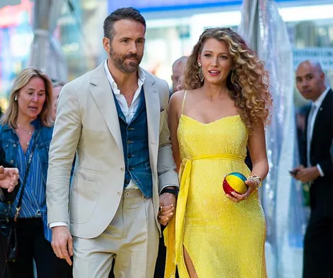 A couple walking, the man in a beige suit and the woman in a yellow dress holding a colorful ball.