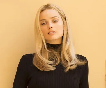 Blonde woman in a black top against a pale background, appearing relaxed and confident.