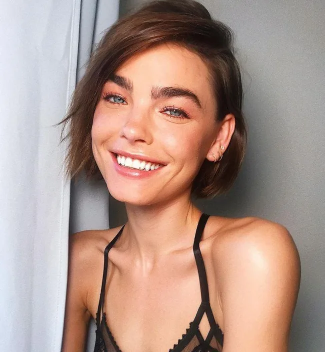 A woman with short brown hair smiling, wearing a black strappy top.