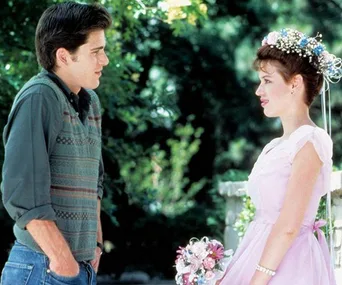 A girl in a pink dress with flowers in her hair looks at a boy in a gray sweater outside.