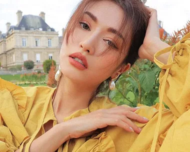 Woman in a yellow outfit posing outdoors, with a historic building in the background.