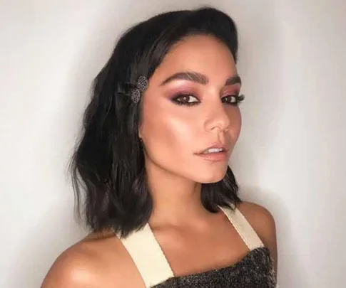 Woman with wavy, shoulder-length hair wearing a butterfly hair clip and sleeveless top, featuring a glam makeup look.