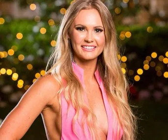 Woman in pink dress smiling outdoors with blurred lights in background.