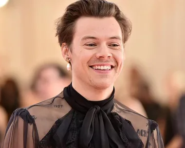 A person smiling, wearing a sheer black outfit with pearl earring, attending an event.