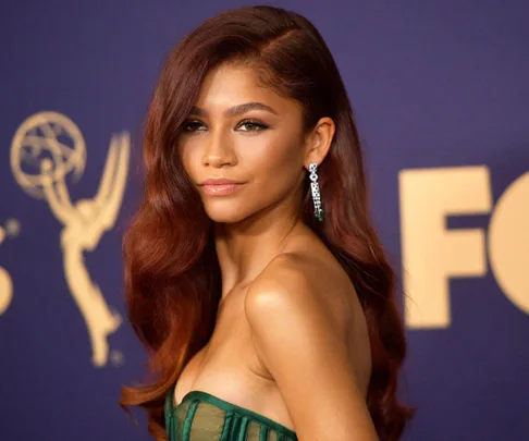 "Zendaya at the 2019 Emmys in a green dress, standing against a backdrop with Emmy logo."