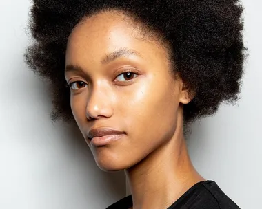 Person with natural hair displaying healthy, glowing skin against a neutral background.