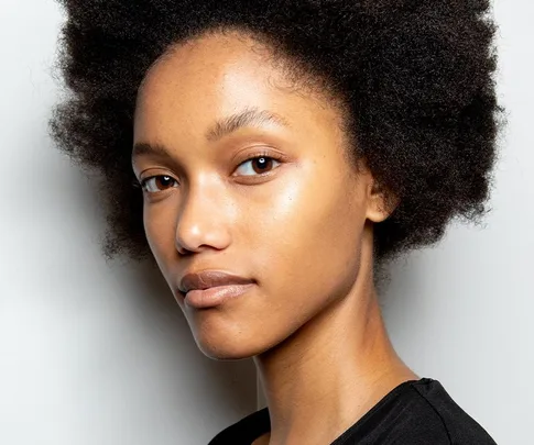 Person with natural hair displaying healthy, glowing skin against a neutral background.