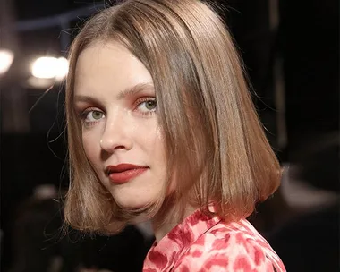 A woman with a sleek, shoulder-length bob hairstyle and red blouse, looking over her shoulder.