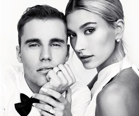 A couple posing closely in a black and white portrait, both wearing stylish outfits with rings visible.