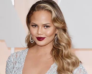 Woman with long wavy hair and red lipstick in a sparkly dress smiling at an event.