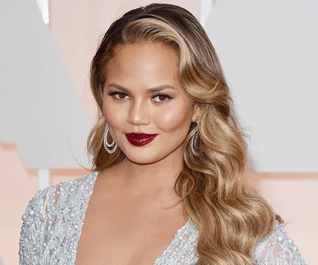 Woman with long wavy hair and red lipstick in a sparkly dress smiling at an event.