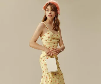 Woman in floral dress holding a small white handbag, wearing a pink feathered headband and earrings.