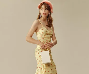 Woman in floral dress holding a small white handbag, wearing a pink feathered headband and earrings.