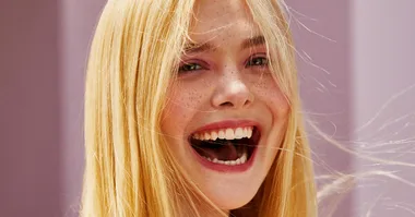 A person with long blonde hair and freckles smiling widely, showing excitement and joy.