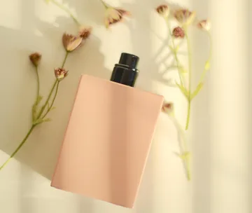 Peach perfume bottle amidst delicate dried flowers on a light background.