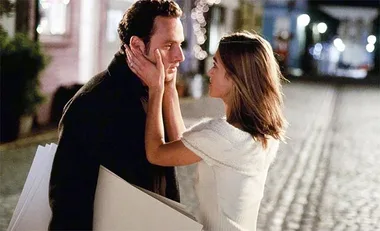 A romantic evening scene with a woman holding a man's face on a cobblestone street.