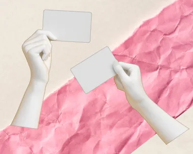 Two hands holding blank cards against a crumpled pink and beige paper background.