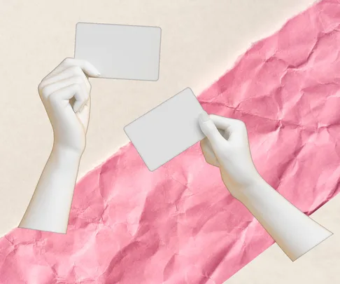 Two hands holding blank cards against a crumpled pink and beige paper background.