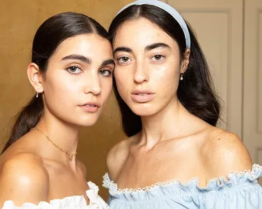 Two women with summer hairstyles and off-the-shoulder tops pose against a neutral background.