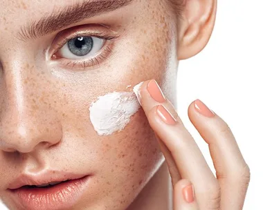 Close-up of a person applying cream to their cheek, focusing on skincare.