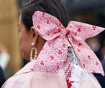 Woman wearing large red and white floral bow with pearl hoop earrings on Stakes Day 2019.