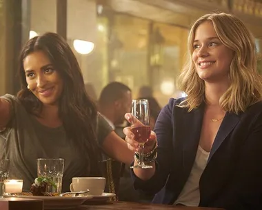 Two women sitting at a table in a restaurant, smiling and raising wine glasses.